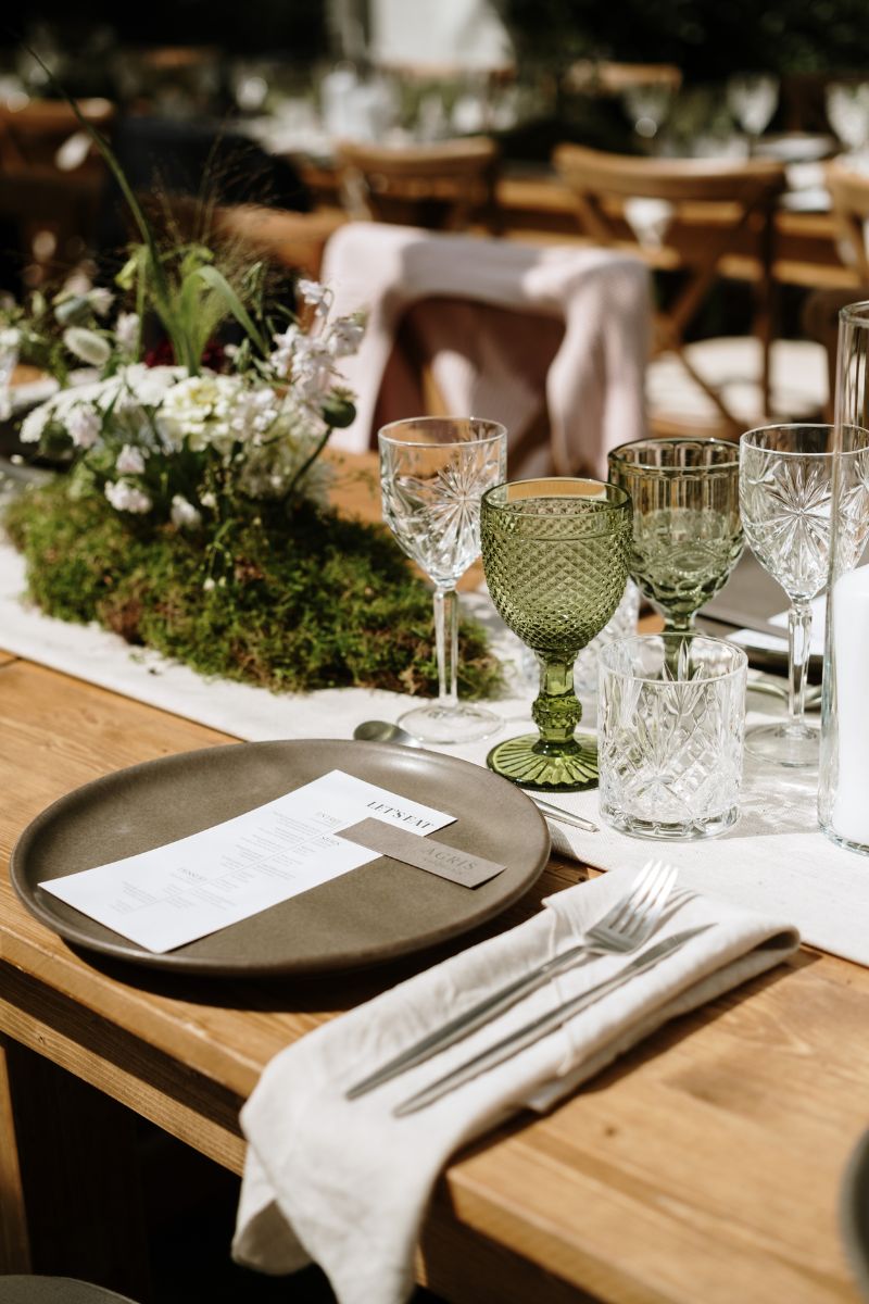 Grønt vinglas til bryllup og sandfarvet serviet på plankebord